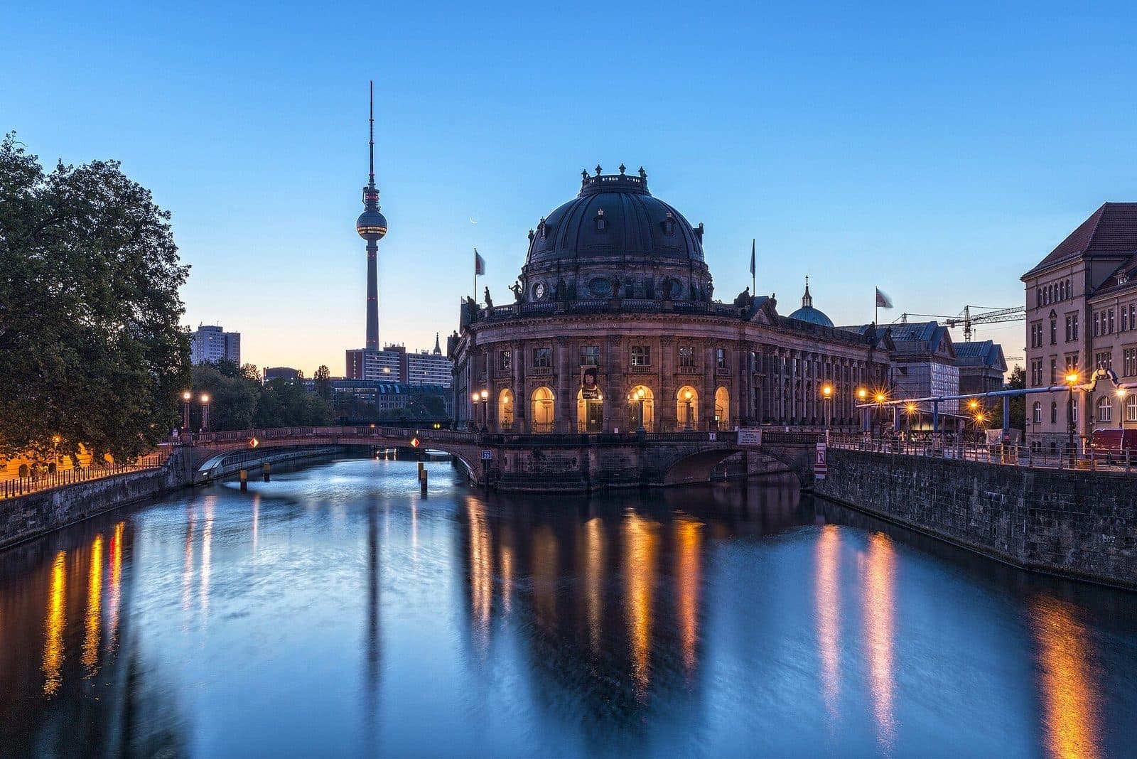 Het verlichte Bode-Museum en de Fernsehturm bij zonsopkomst, weerspiegeld in de Spree