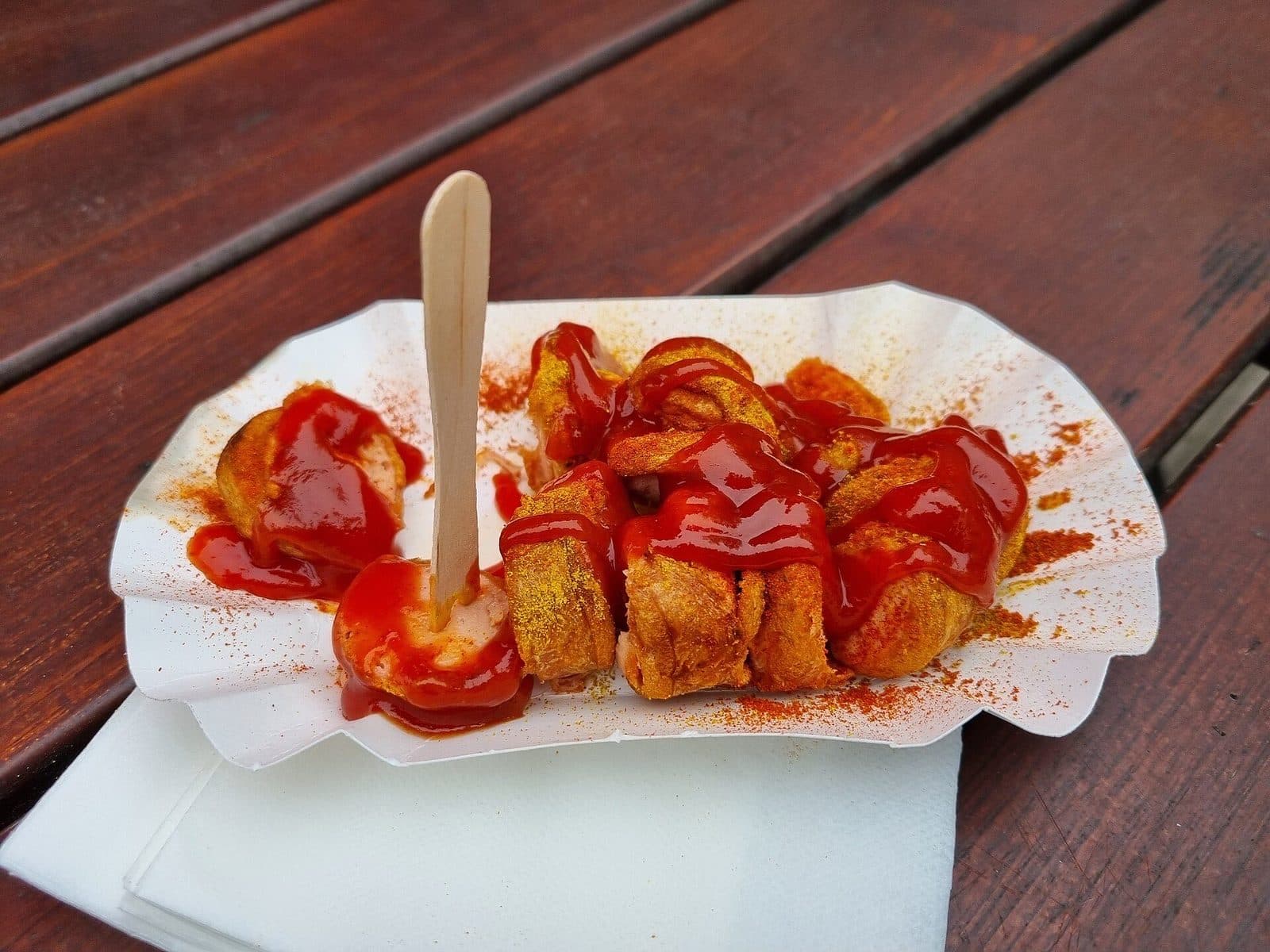 Een bakje currywurst met curryketchup en kerriepoeder op een houten tafel