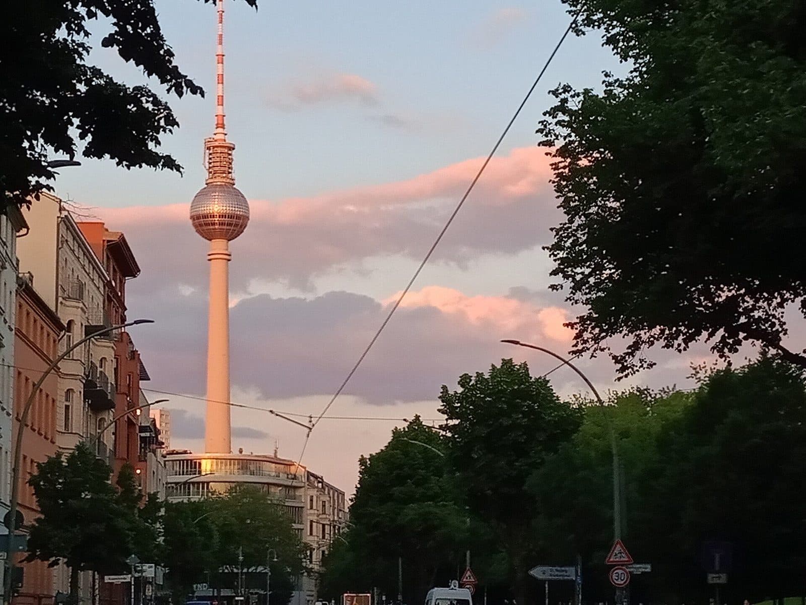 De Fernsehturm steekt boven de bomen en gevels uit tegen een roze avondlucht