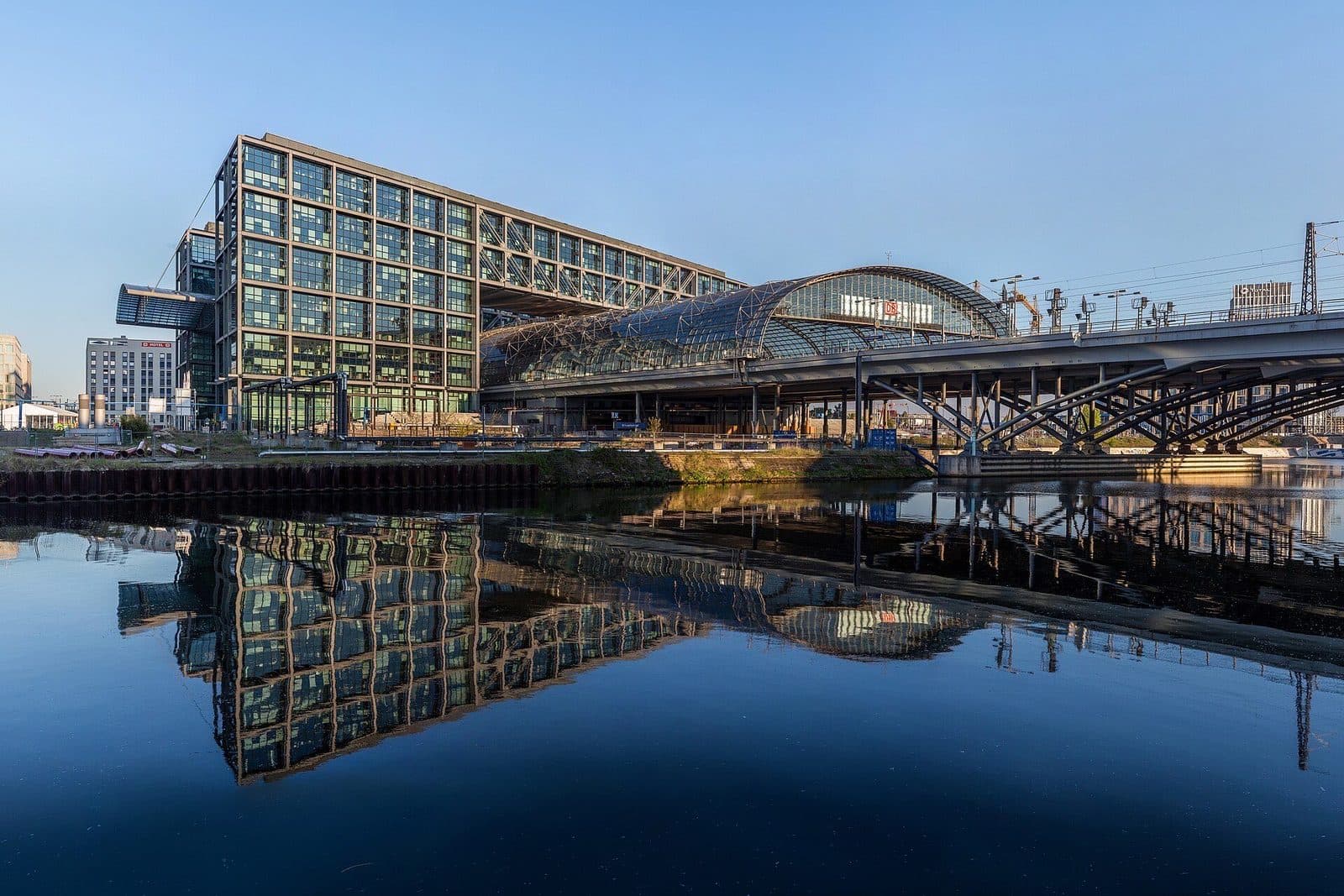 Berlin Hauptbahnhof met de glazen overkapping, weerspiegeld in de Spree op een heldere ochtend
