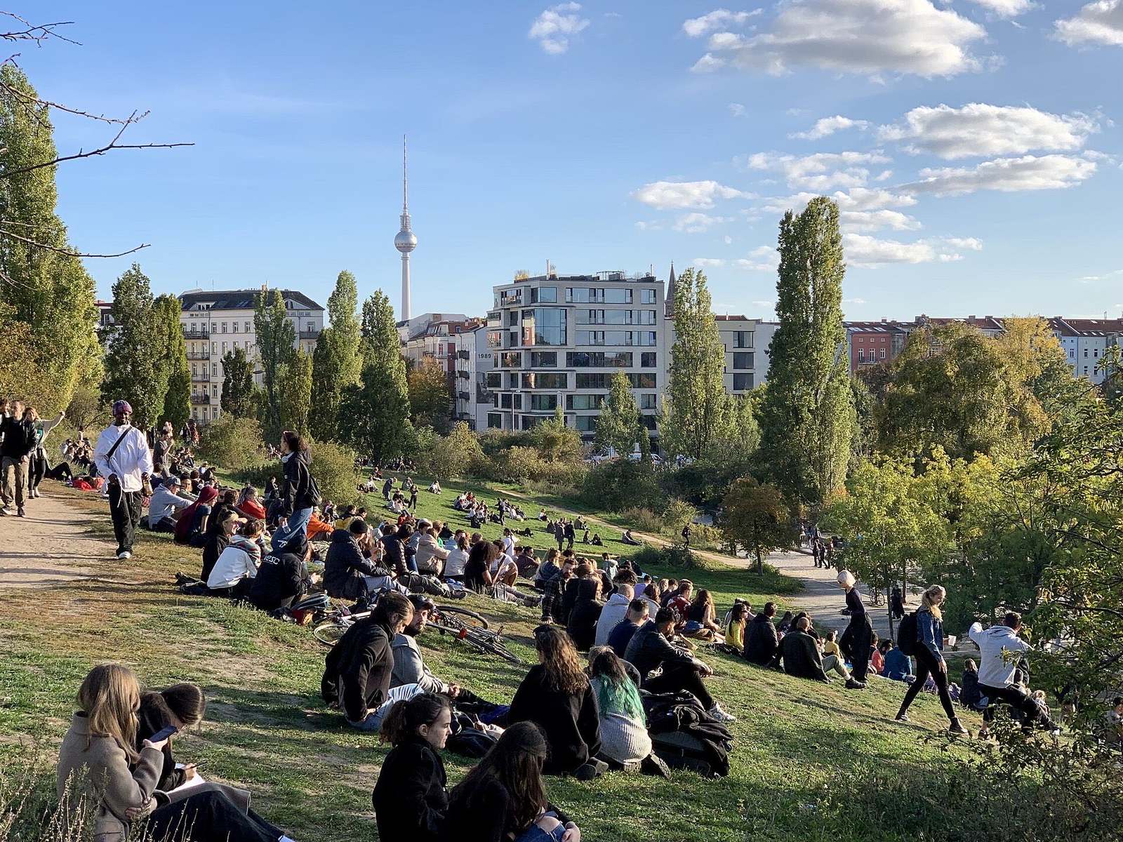 Mensen zitten op de grasheuvel van het Mauerpark in Prenzlauer Berg, met de Fernsehturm in de verte