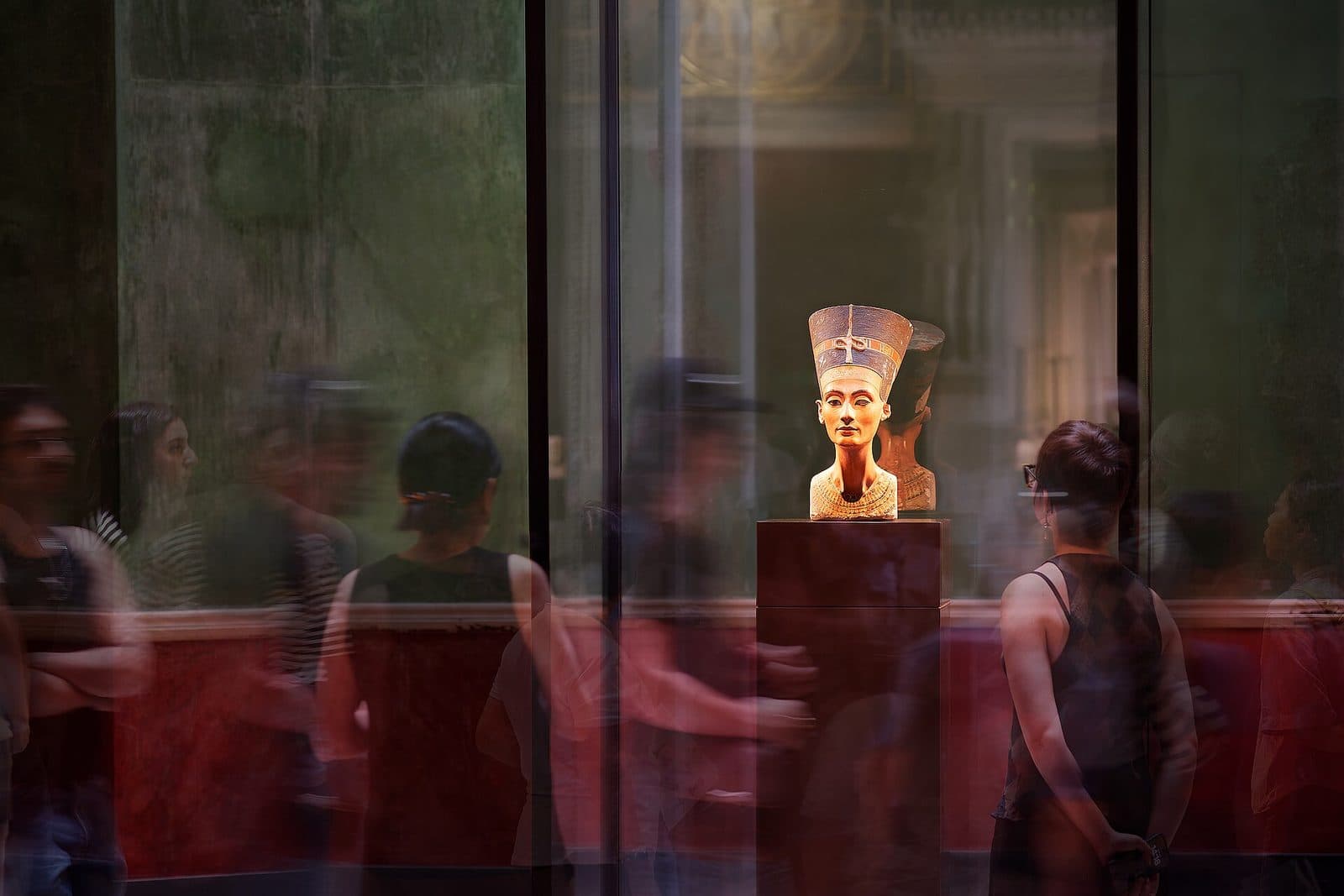 De buste van Nefertiti in het Neues Museum, omringd door bezoekers in een zaal met rode wanden