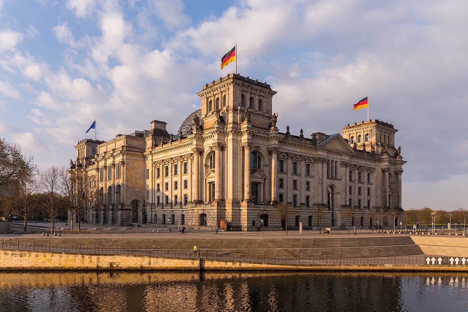 Het Rijksdaggebouw met Duitse vlaggen in het late middaglicht, gezien vanaf de oever van de Spree
