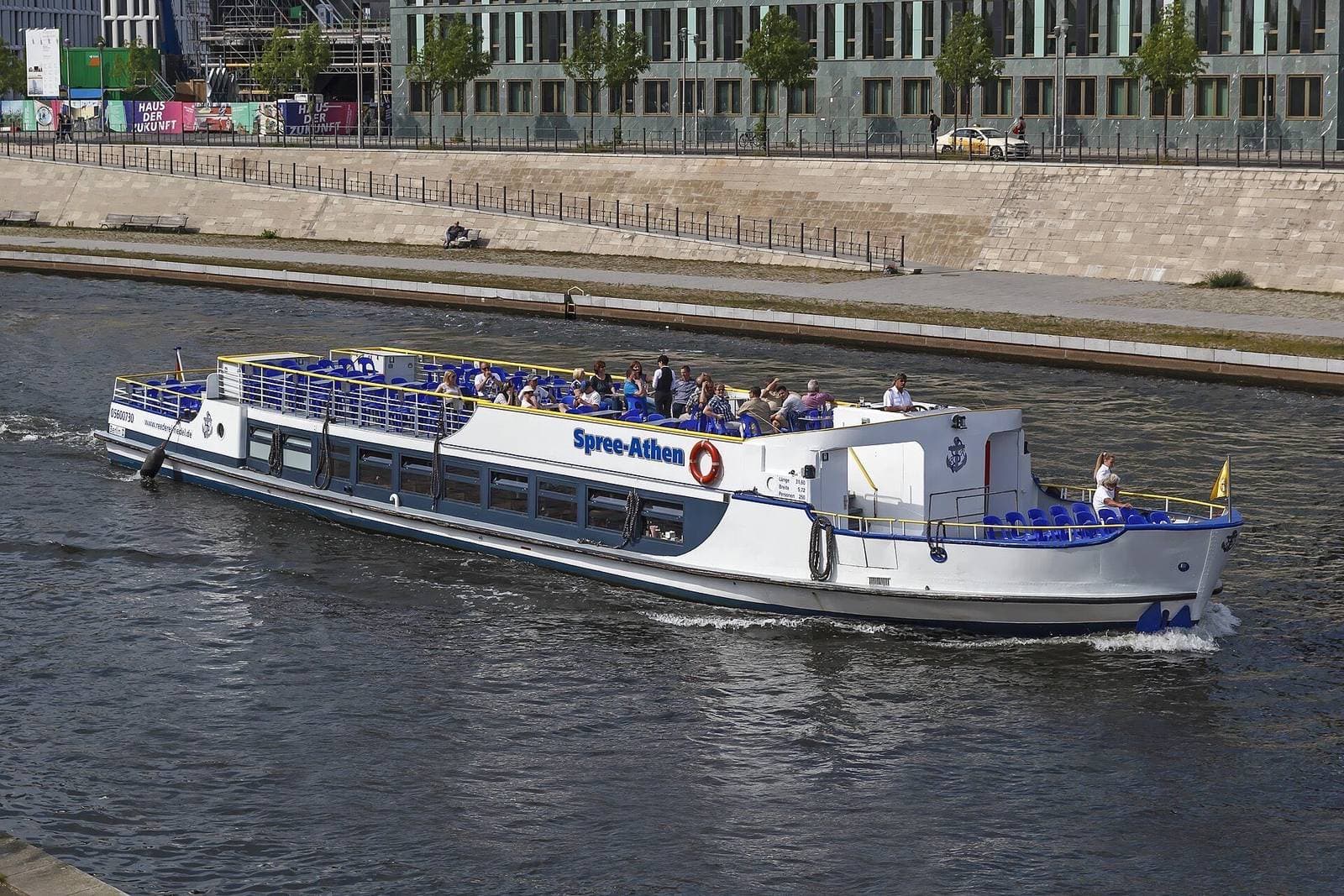Een rondvaartboot met passagiers op het bovendek vaart over de Spree langs de kade van de regeringswijk