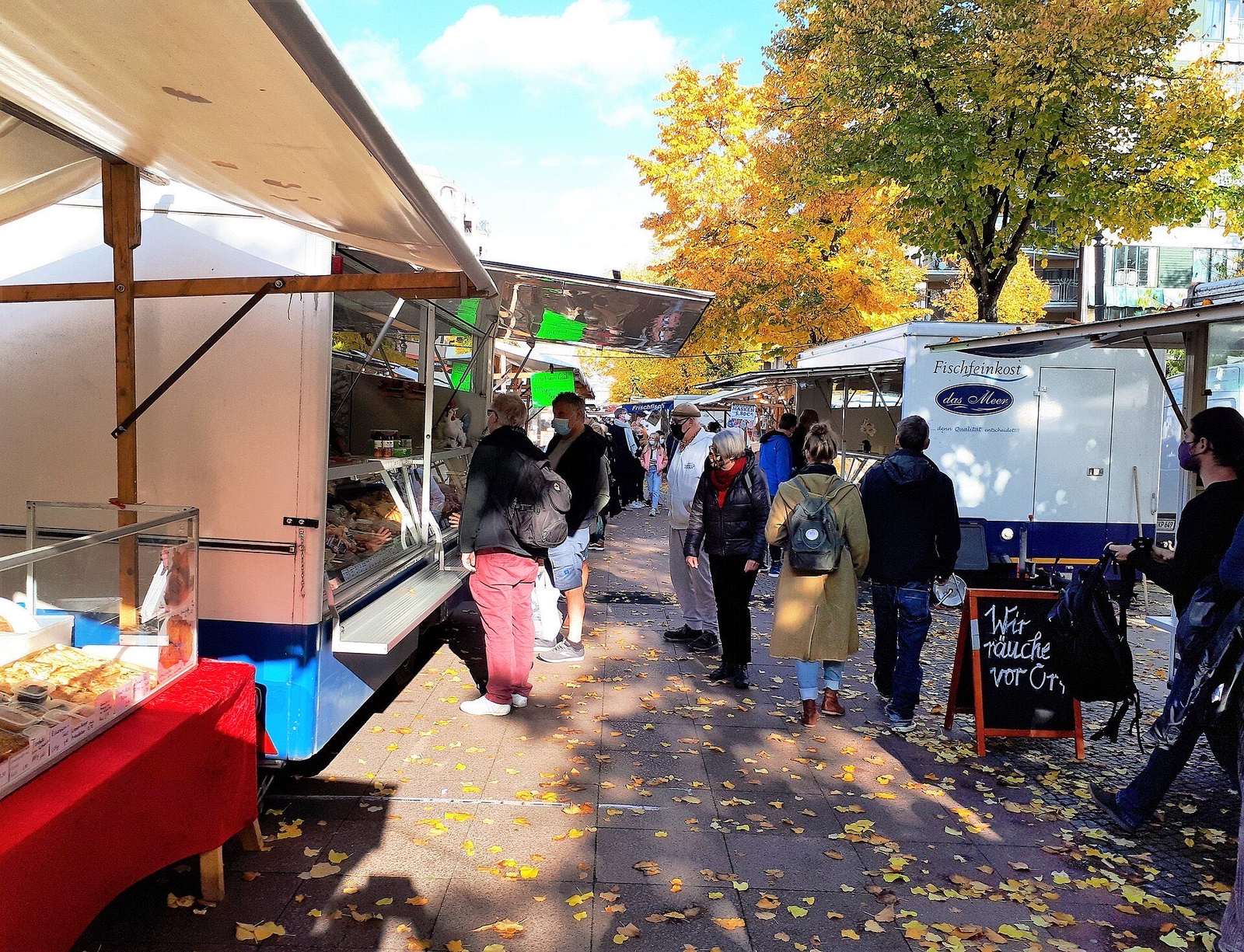 Bezoekers lopen tussen de kramen van de markt op de Winterfeldtplatz in Schöneberg, onder gele herfstbomen